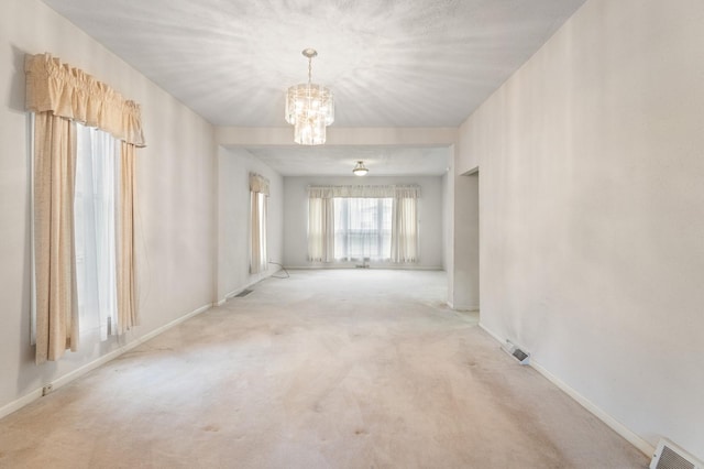 carpeted spare room with an inviting chandelier