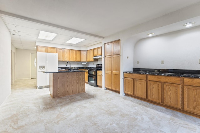 kitchen with a paneled ceiling, white refrigerator with ice dispenser, a center island with sink, sink, and black gas range oven