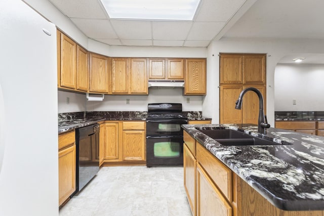 kitchen with black appliances, a paneled ceiling, sink, and dark stone counters