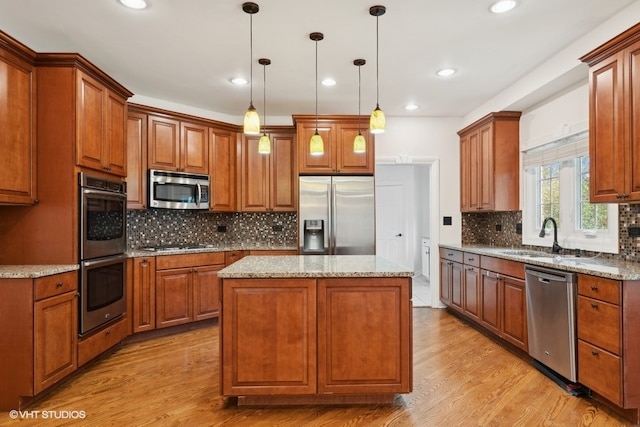 kitchen with tasteful backsplash, a kitchen island, light wood-type flooring, pendant lighting, and stainless steel appliances