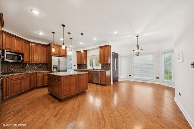 kitchen with appliances with stainless steel finishes, a kitchen island, light wood-type flooring, and pendant lighting