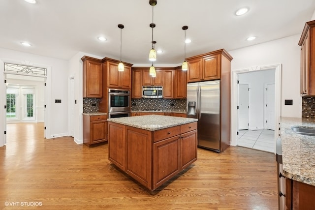 kitchen with decorative backsplash, hanging light fixtures, light stone countertops, light wood-type flooring, and appliances with stainless steel finishes