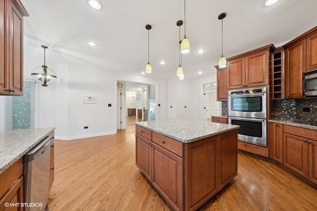 kitchen featuring a kitchen island, decorative light fixtures, light wood-type flooring, appliances with stainless steel finishes, and light stone counters