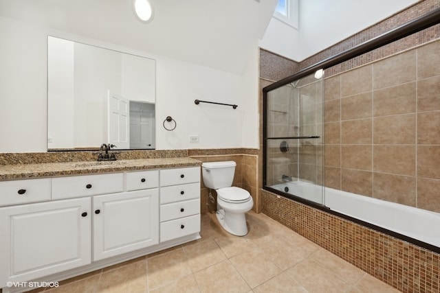 full bathroom with a skylight, shower / bath combination with glass door, toilet, vanity, and tile patterned flooring