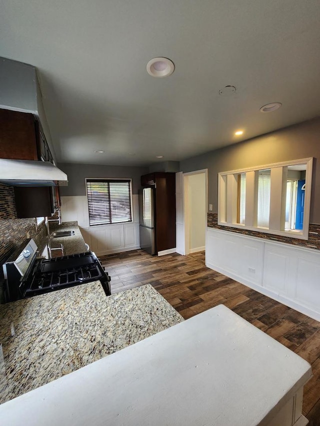 kitchen featuring range, dark brown cabinetry, dark wood-type flooring, decorative backsplash, and stainless steel refrigerator