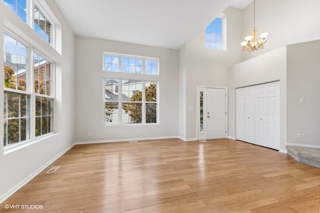 foyer with a towering ceiling, a healthy amount of sunlight, a notable chandelier, and light hardwood / wood-style floors