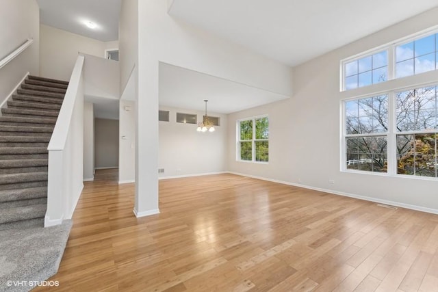 unfurnished living room with a towering ceiling, a notable chandelier, and light wood-type flooring