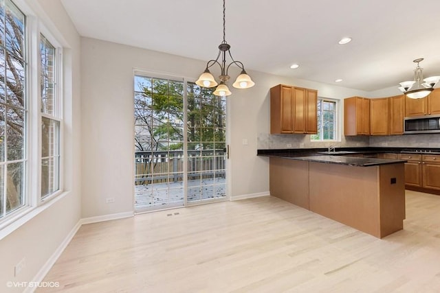 kitchen with backsplash, hanging light fixtures, kitchen peninsula, an inviting chandelier, and light hardwood / wood-style flooring