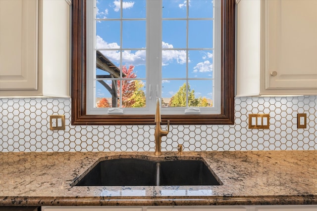 interior details with white cabinetry, stone countertops, decorative backsplash, and sink