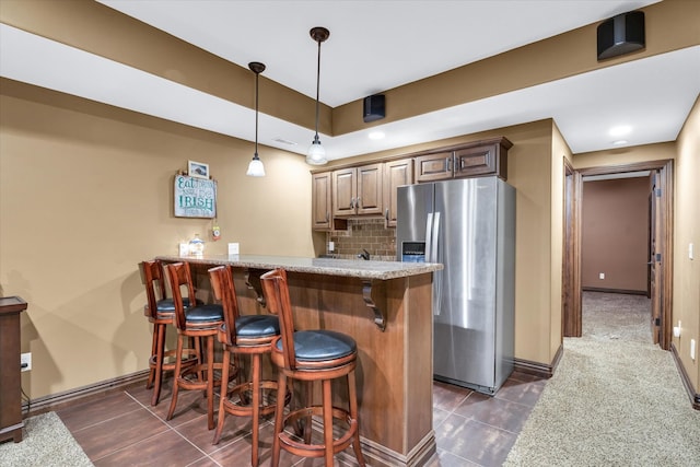 bar featuring dark tile patterned floors, stainless steel fridge, pendant lighting, light stone counters, and tasteful backsplash