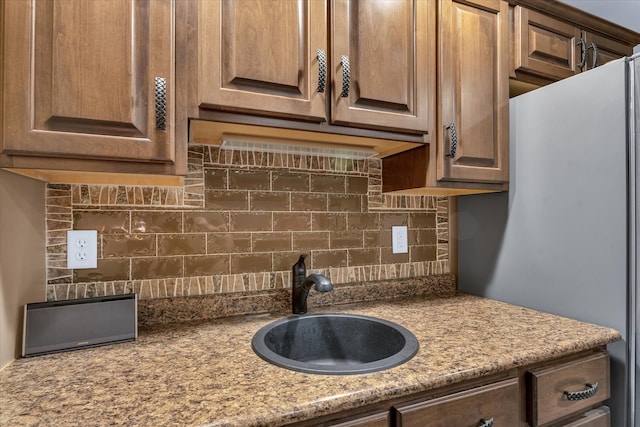 kitchen featuring white fridge, light stone countertops, decorative backsplash, and sink