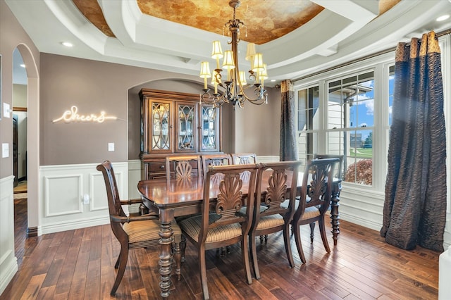 dining space with a notable chandelier, ornamental molding, dark wood-type flooring, and a raised ceiling