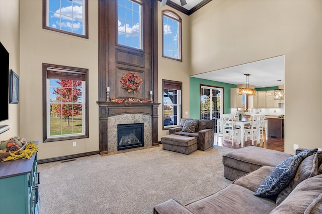 carpeted living room featuring a notable chandelier, a premium fireplace, a high ceiling, and ornamental molding