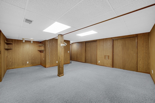 basement with a drop ceiling, light carpet, and wood walls