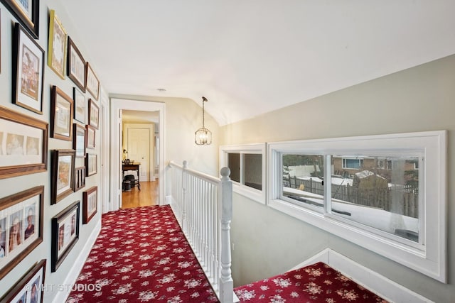 corridor with vaulted ceiling, carpet floors, and a chandelier