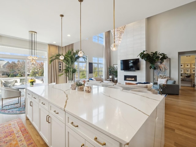 kitchen featuring light stone counters, a fireplace, a center island, white cabinetry, and hanging light fixtures