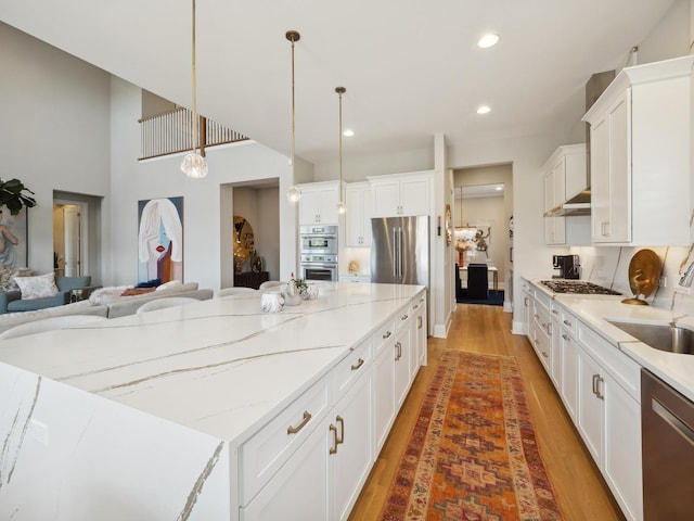 kitchen with white cabinets, a spacious island, sink, decorative light fixtures, and stainless steel appliances