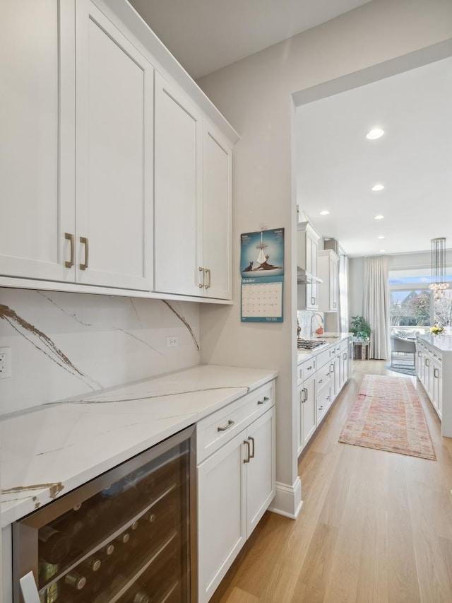 kitchen with wine cooler, decorative backsplash, light wood-type flooring, light stone counters, and white cabinetry