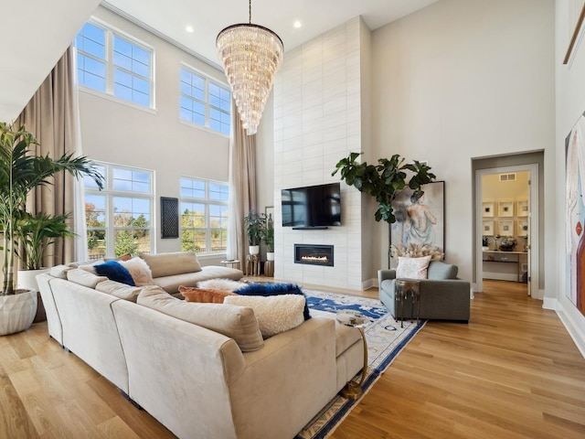 living room with a tiled fireplace, light hardwood / wood-style flooring, a towering ceiling, and a chandelier