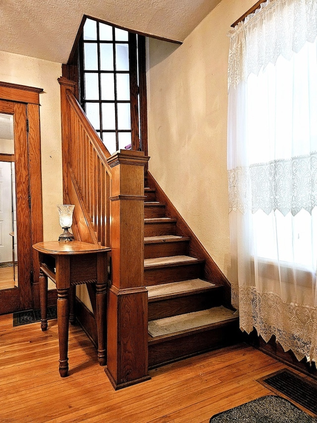 stairway featuring a textured ceiling, hardwood / wood-style flooring, and a healthy amount of sunlight