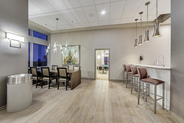 interior space with a towering ceiling, a drop ceiling, hanging light fixtures, and light wood-type flooring