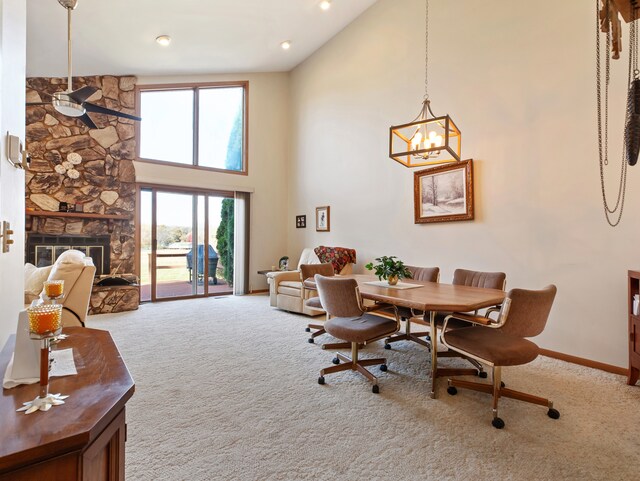 carpeted dining room with a fireplace, a towering ceiling, and ceiling fan with notable chandelier