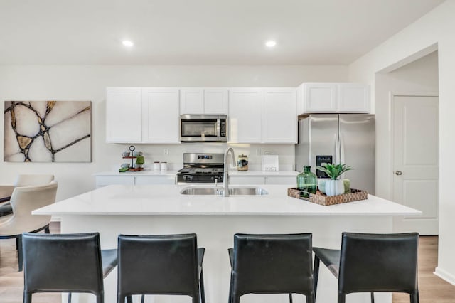 kitchen with a center island with sink, white cabinets, stainless steel appliances, and hardwood / wood-style floors