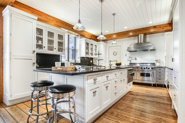 kitchen featuring wall chimney range hood, light hardwood / wood-style flooring, white cabinetry, and high end range