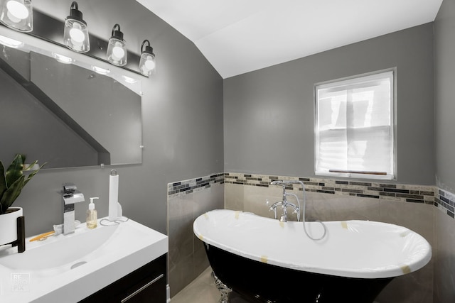 bathroom featuring tile walls, a washtub, vanity, and vaulted ceiling