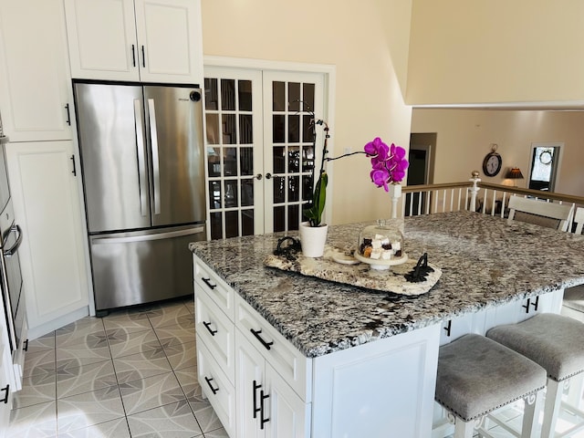 kitchen featuring a kitchen island, white cabinets, dark stone countertops, stainless steel refrigerator, and light tile patterned floors