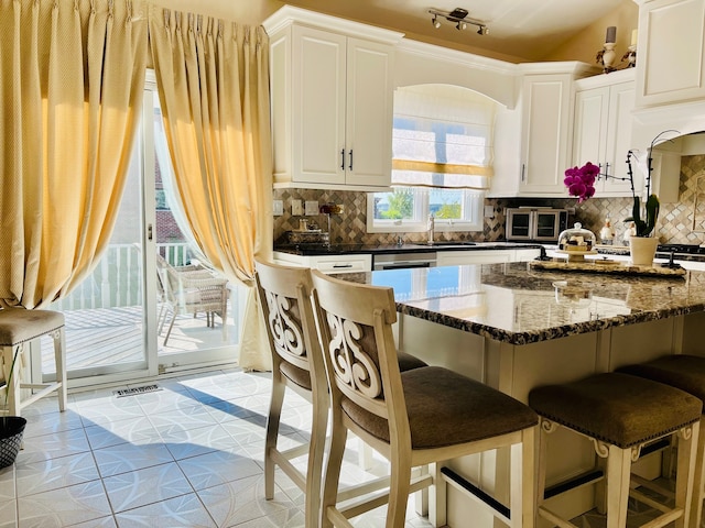 kitchen with sink, backsplash, rail lighting, dark stone counters, and white cabinets