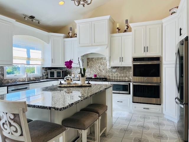 kitchen with vaulted ceiling, appliances with stainless steel finishes, decorative backsplash, and white cabinetry