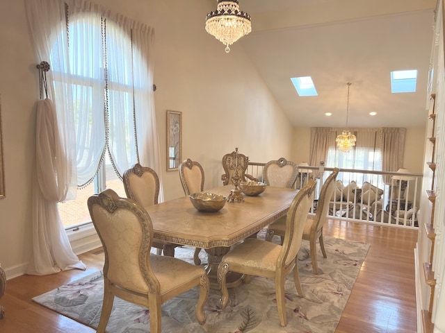 dining room featuring high vaulted ceiling, hardwood / wood-style flooring, an inviting chandelier, and a skylight