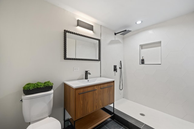 bathroom with tile patterned flooring, vanity, tiled shower, and toilet