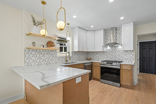 kitchen featuring wall chimney exhaust hood, sink, stainless steel gas range oven, light stone counters, and white cabinets