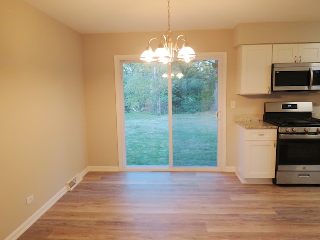 kitchen with appliances with stainless steel finishes, decorative light fixtures, light wood-type flooring, and white cabinets