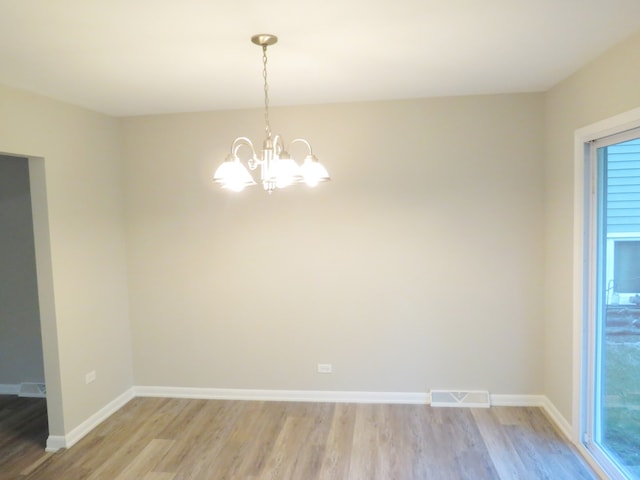 spare room with a notable chandelier and light wood-type flooring