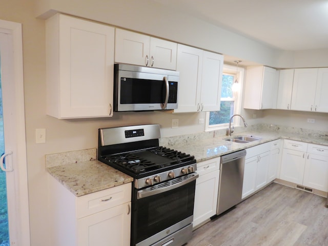 kitchen with light hardwood / wood-style flooring, stainless steel appliances, sink, white cabinets, and light stone counters