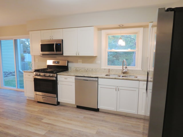 kitchen with white cabinets, light hardwood / wood-style flooring, sink, decorative light fixtures, and stainless steel appliances