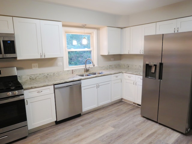 kitchen featuring appliances with stainless steel finishes, sink, white cabinetry, light hardwood / wood-style floors, and decorative light fixtures