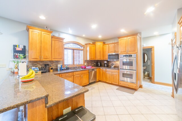 kitchen featuring sink, backsplash, kitchen peninsula, stainless steel appliances, and dark stone counters