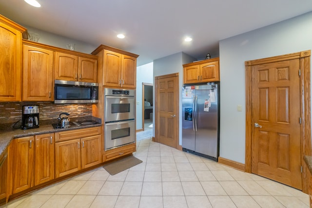 kitchen with dark stone countertops, backsplash, appliances with stainless steel finishes, and light tile patterned floors