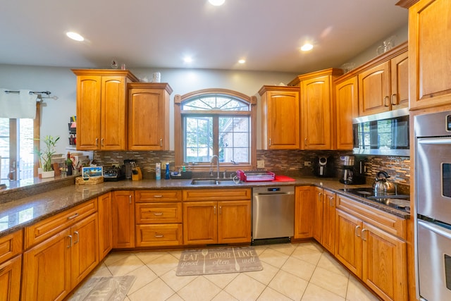 kitchen with sink, appliances with stainless steel finishes, a healthy amount of sunlight, and dark stone counters