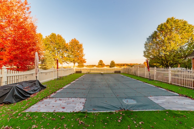 pool at dusk with a patio and a lawn