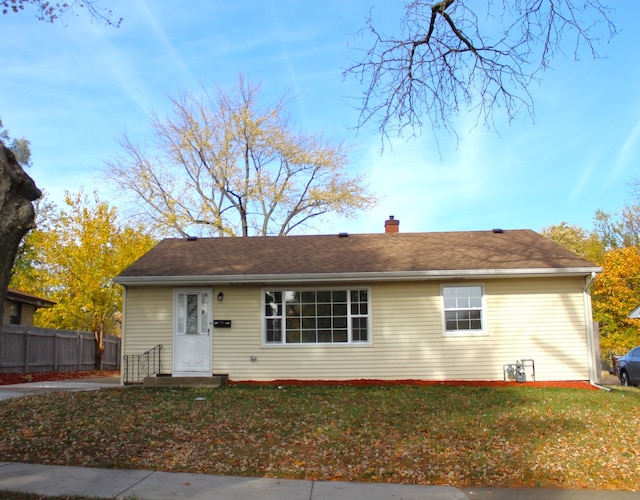 ranch-style home with a chimney, a front yard, and fence