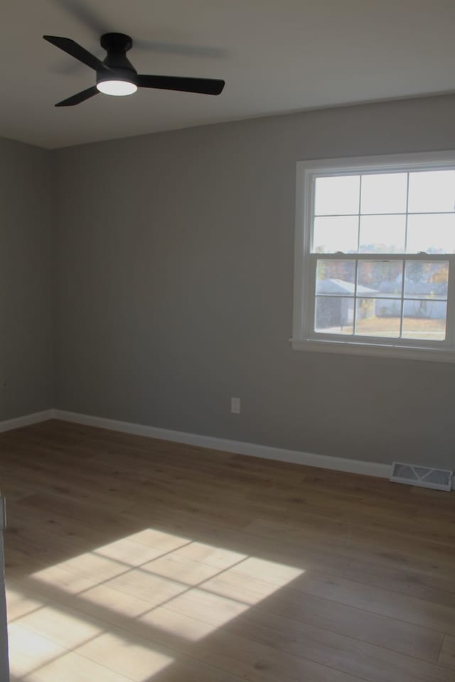 empty room featuring light wood finished floors, baseboards, visible vents, and a ceiling fan