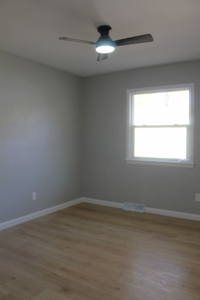 empty room with light wood finished floors, baseboards, visible vents, and a ceiling fan