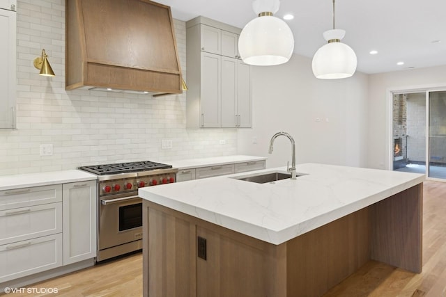 kitchen featuring premium range hood, designer range, pendant lighting, an island with sink, and sink