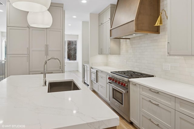 kitchen with gray cabinetry, stainless steel appliances, sink, and premium range hood