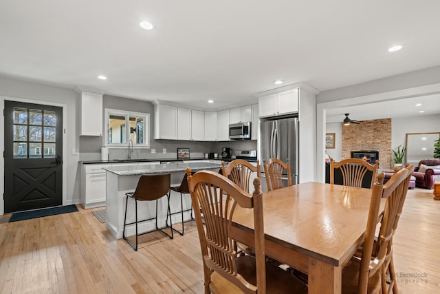 dining area featuring a large fireplace, ceiling fan, sink, and light hardwood / wood-style floors